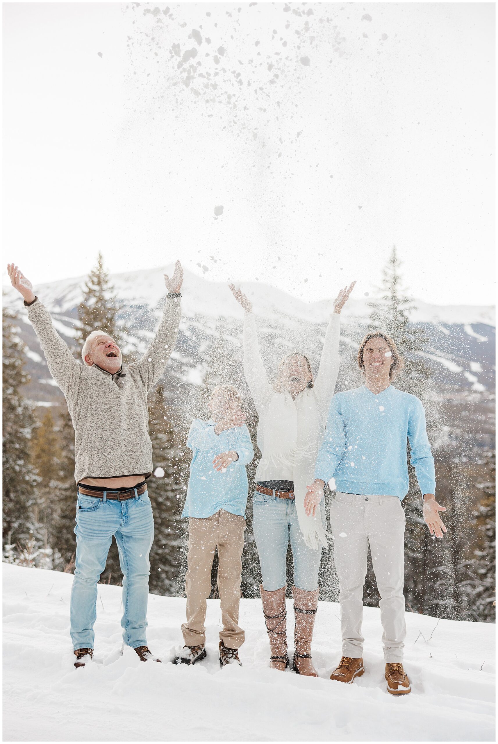 Family of 4 dressed in white, blue, and khaki throwing snow in the air during their winter family photos in Breckenridge