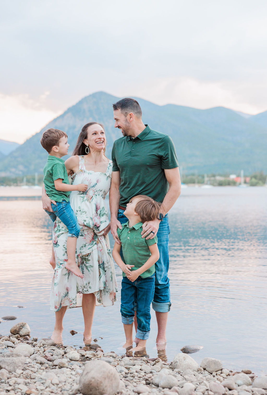 Happy parents explore an alpine lake at sunset with their matching 2 toddler sons