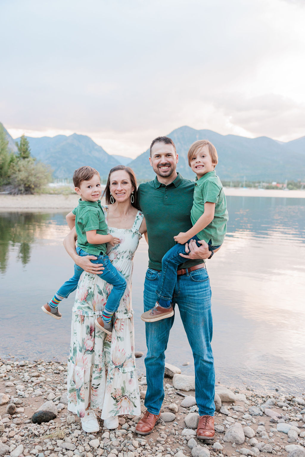 Happy mom and dad stand by an alpine lake at sunset holding their 2 toddler sons before finding Best Places to Eat with Kids in Breckenridge