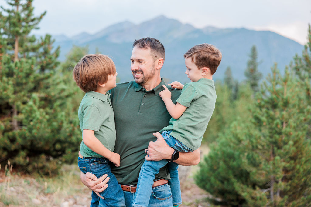 A happy dad in a green polo plays with his 2 matching toddler sons on a mountain trail at sunset before finding Best Places to Eat with Kids in Breckenridge