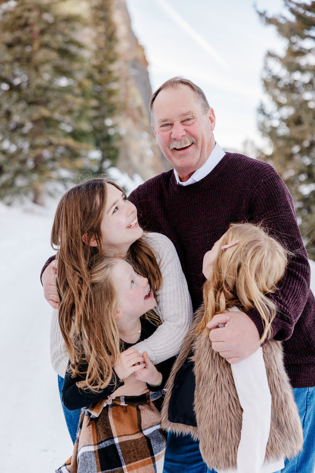 Dad in maroon sweater hugging his three daughters and laughing during Breckenridge Winter Activities