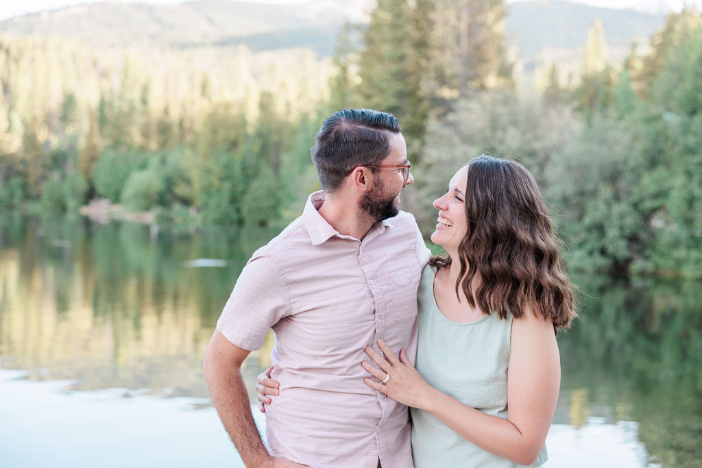 A couple hugs and laughs big by an alpine lake at sunset