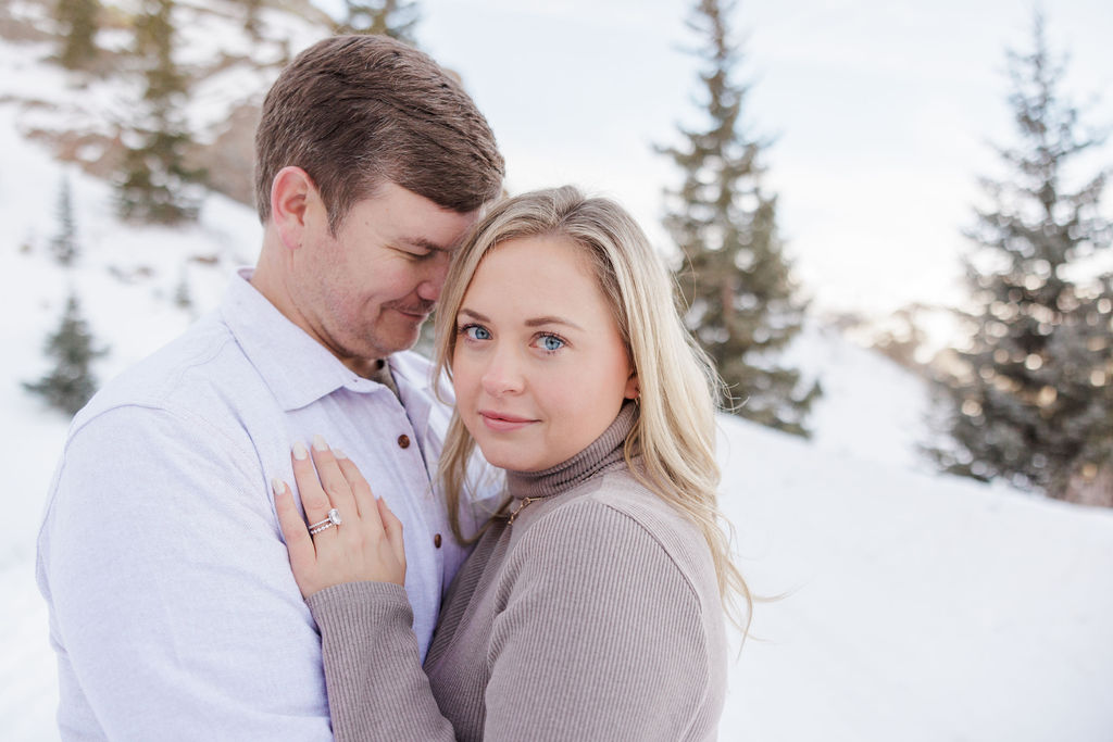 An engaged woman snuggles on the chest of her husband on a snowy hillside at sunset before visiting romantic restaurants breckenridge