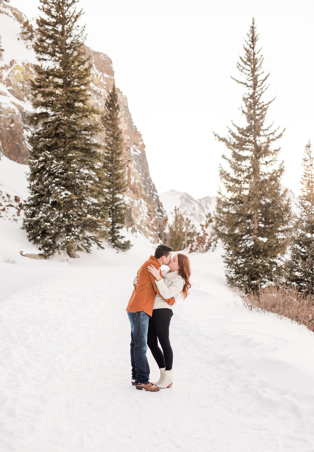 A happy couple kisses on a snowy mountain trail at sunset before visiting romantic restaurants breckenridge