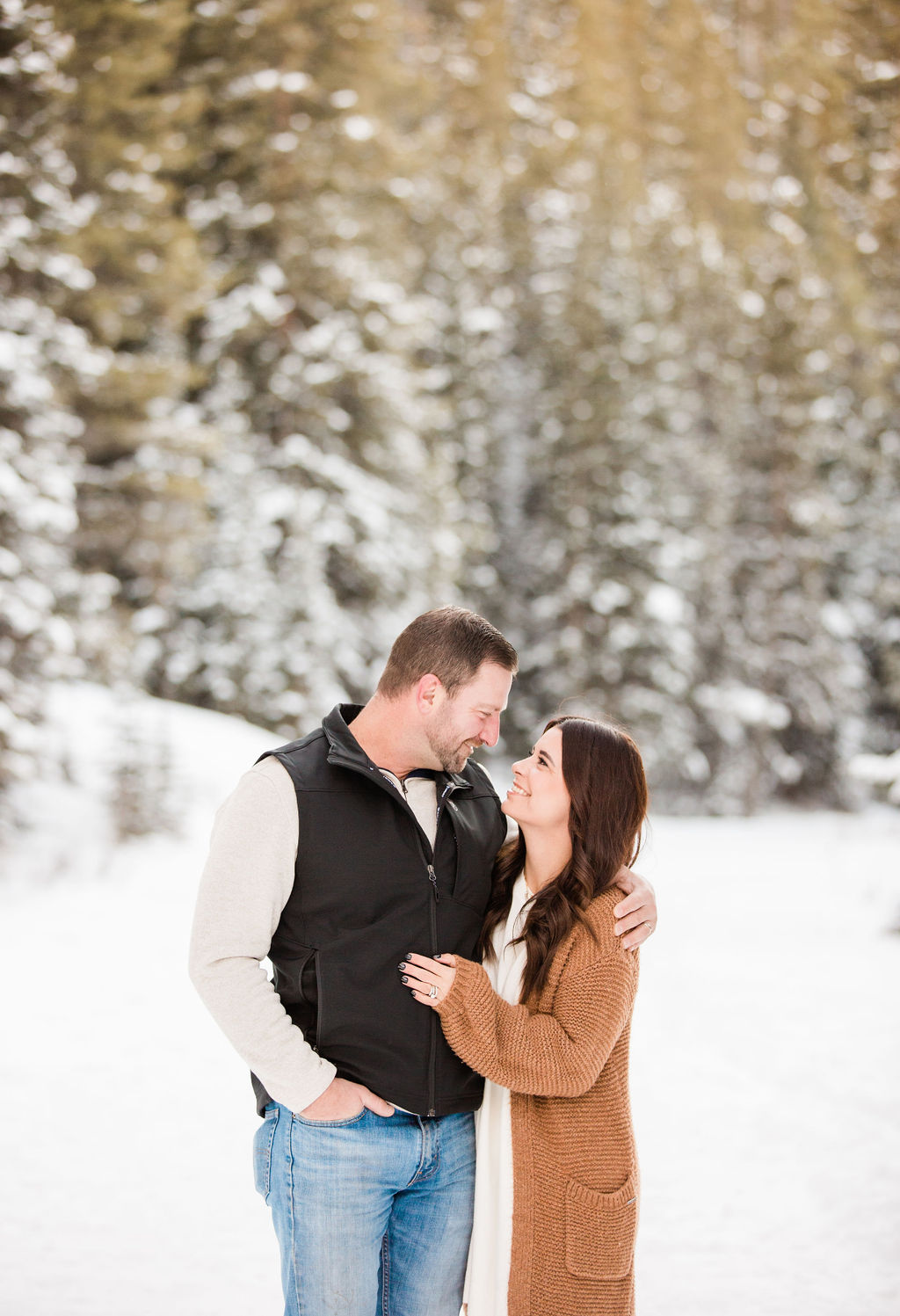 A happy couple snuggles and smiles at each other in a snowy trail before visiting romantic restaurants breckenridge