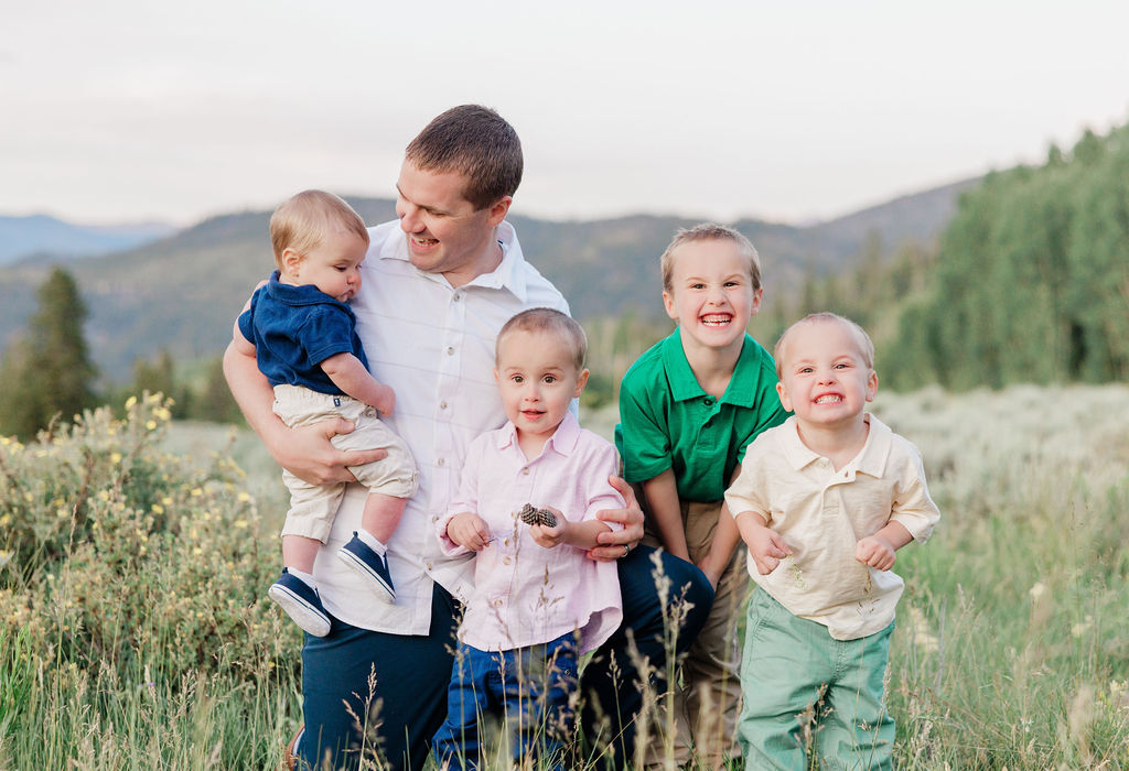 A dad plays with his 4 toddler sons in a mountain meadow at sunset