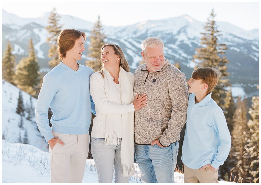 The featured family of four is standing, looking at one another, with Breckenridge Ski Resort behind them