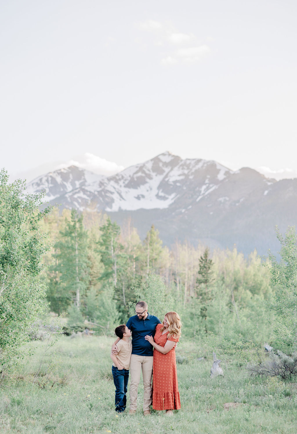 A young boy looks up to mom and dad while hugging them in a mountain meadow after meeting babysitters in breckenridge co