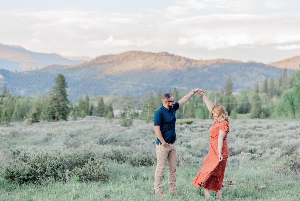 A happy couple dances in a mountain meadow at sunset in a red dress after finding babysitters in breckenridge co