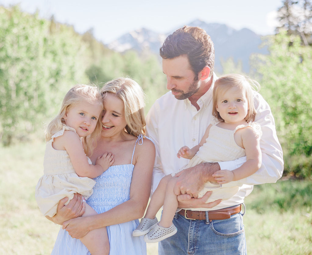 Two happy toddler girls in yellow dresses smile while playing with mom and dad in a mountain trail before visiting the breckenridge children's museum