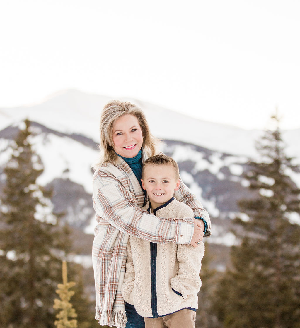 A woman hugs a young boy in a white sweater on a mountain trail