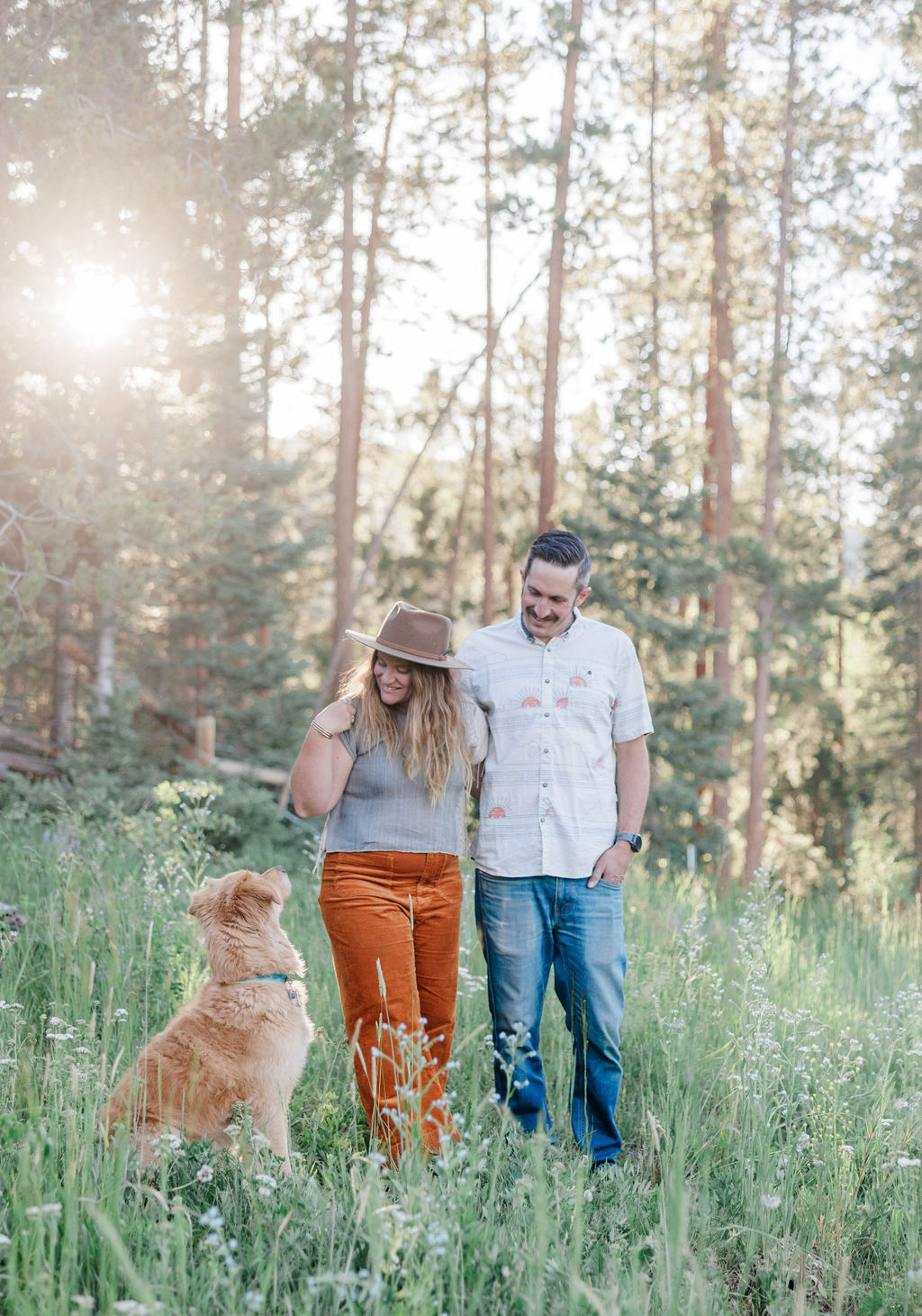 A happy couple explores a mountain meadow with their brown dog at sunset during date ideas in breckenridge