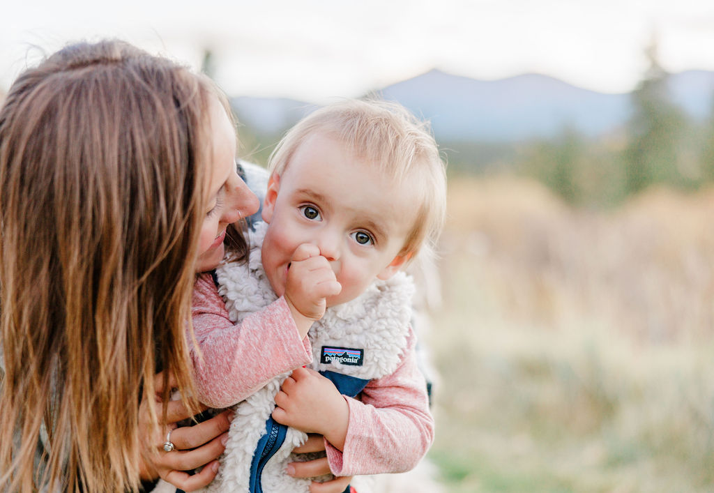 A baby girl snuggles with mom on a mountain trail at sunset