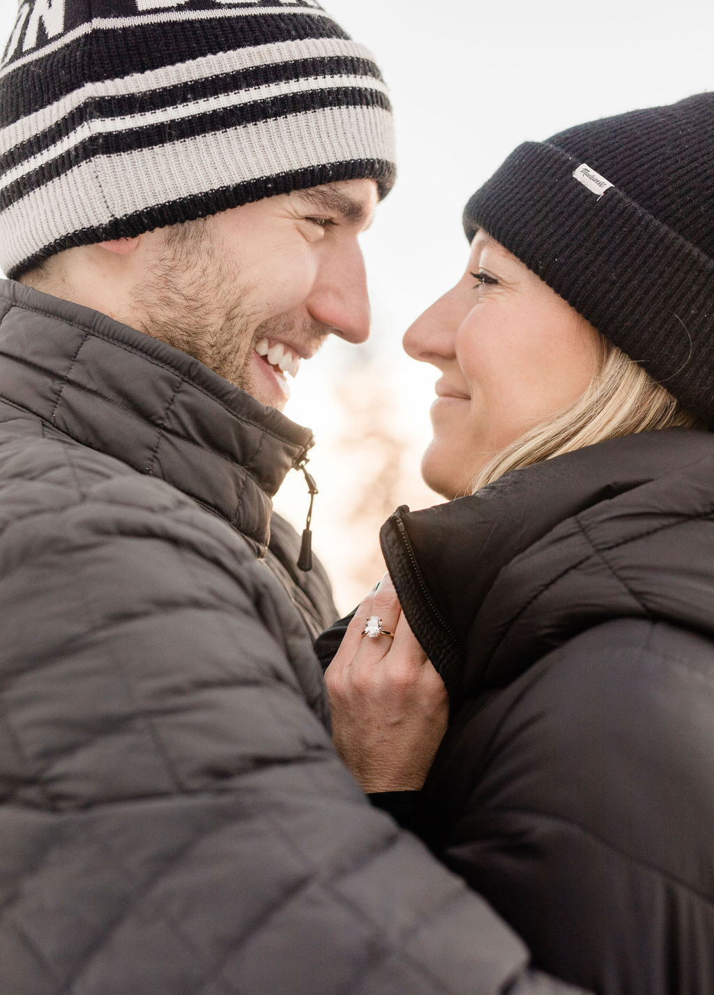 A happy newly engaged couple snuggles in ski jackets and beanies while showing off their ring from jewelry stores in breckenridge colorado