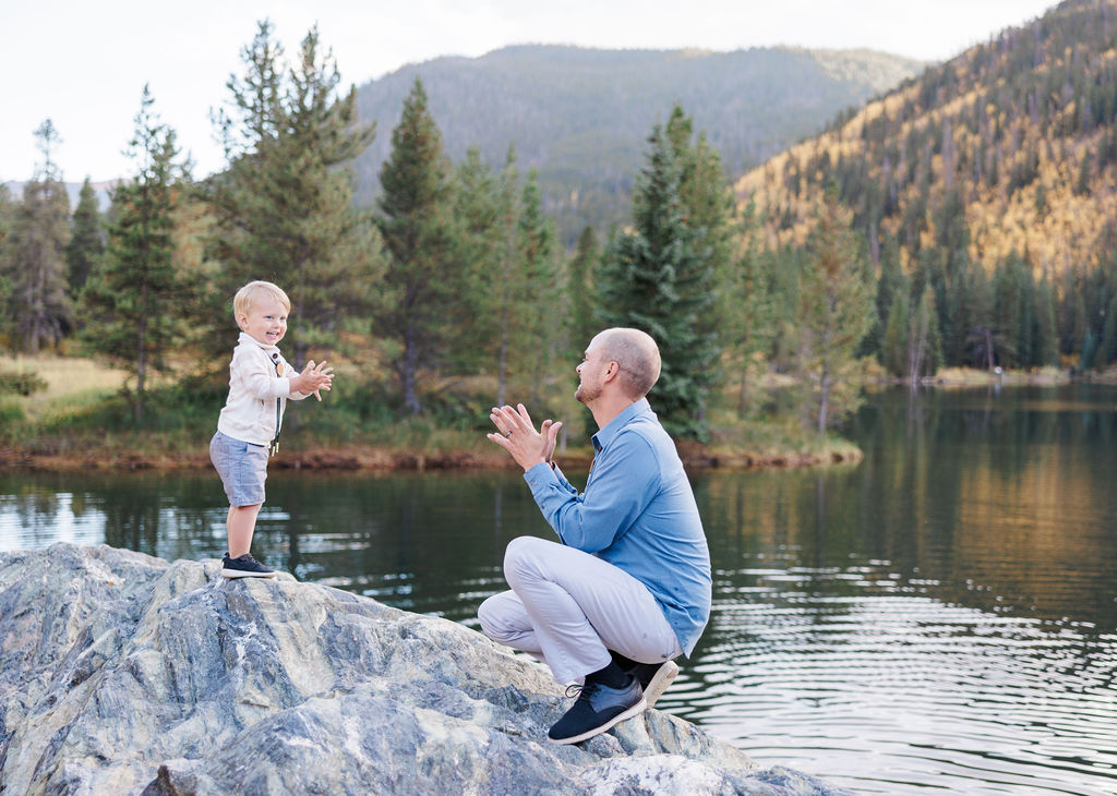 A happy toddler claps with dad while exploring an alpine lake before visiting playgrounds in breckenridge