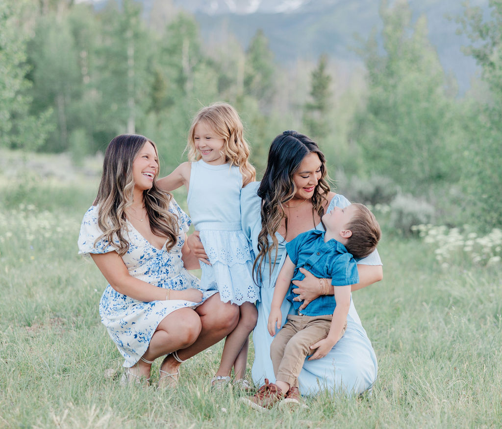 Two women play in the grass with two toddlers on a mountain trail after meeting resort sitters breckenridge