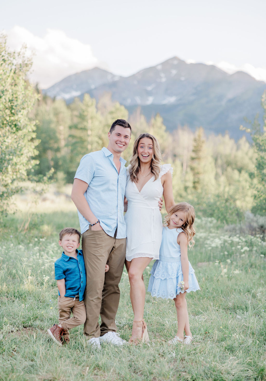 A happy mom and dad smile big while standing in a mountain trail with their toddler son and daughter after using resort sitters breckenridge