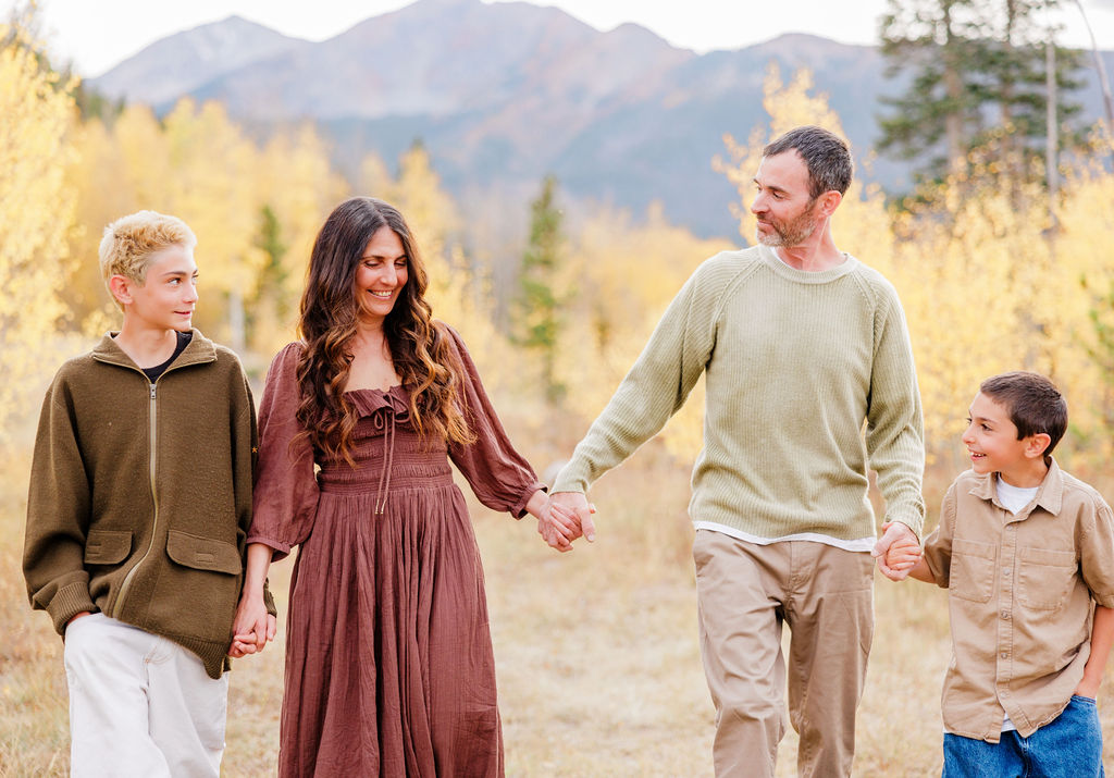 A mom and dad walk in a park holding hands with their teen and young son during things to do with kids in breckenridge