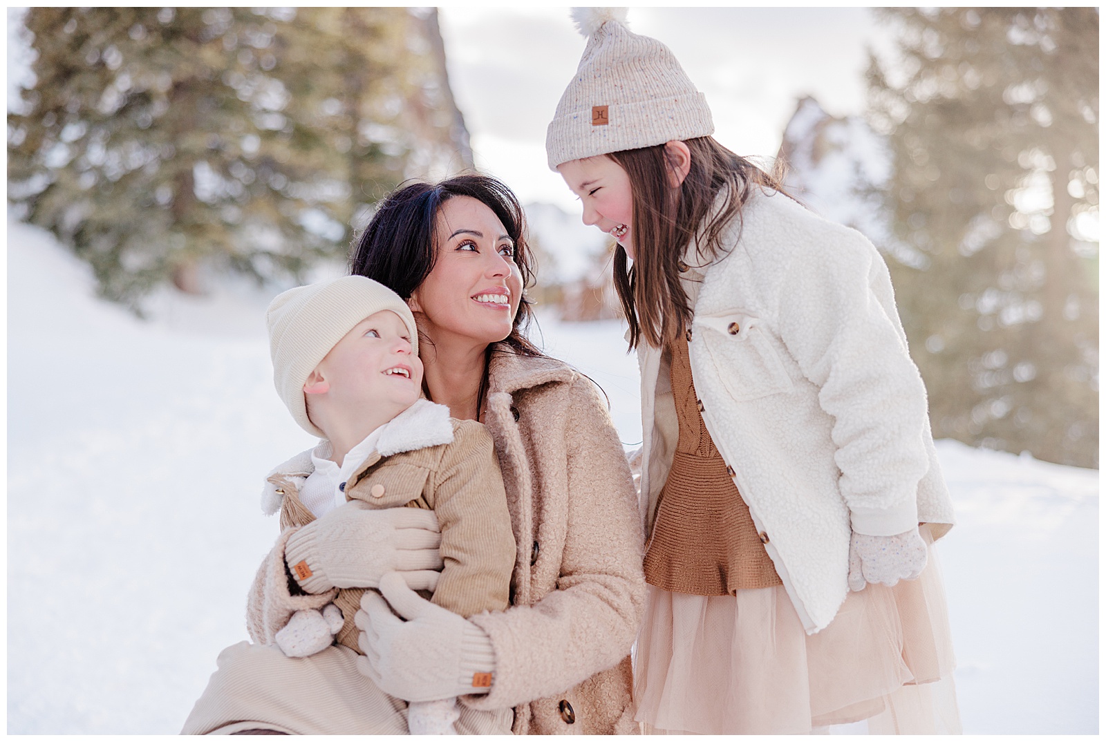 A mom is kneeling down with her two young children. The young boy is on her knee while her daughter is standing next to her. They are amongst a gorgeous snow-filled backdrop. Shot by Breckenridge Photographer Rachel. 