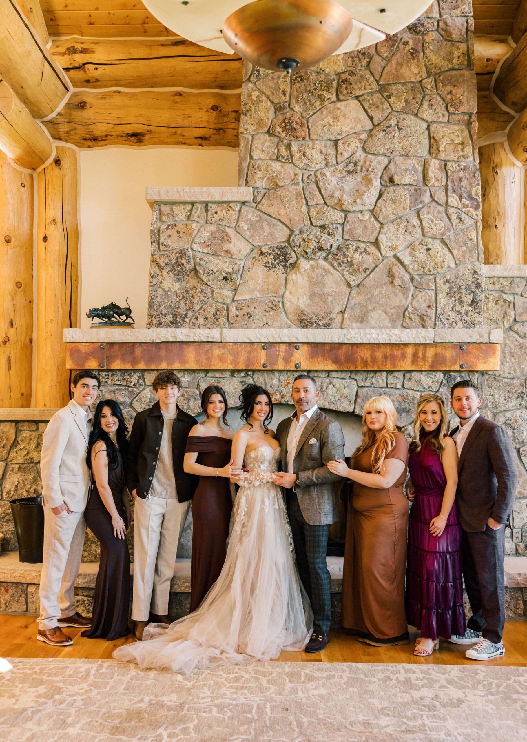 Newlyweds stand in front of a large stone fireplace with their family smiling