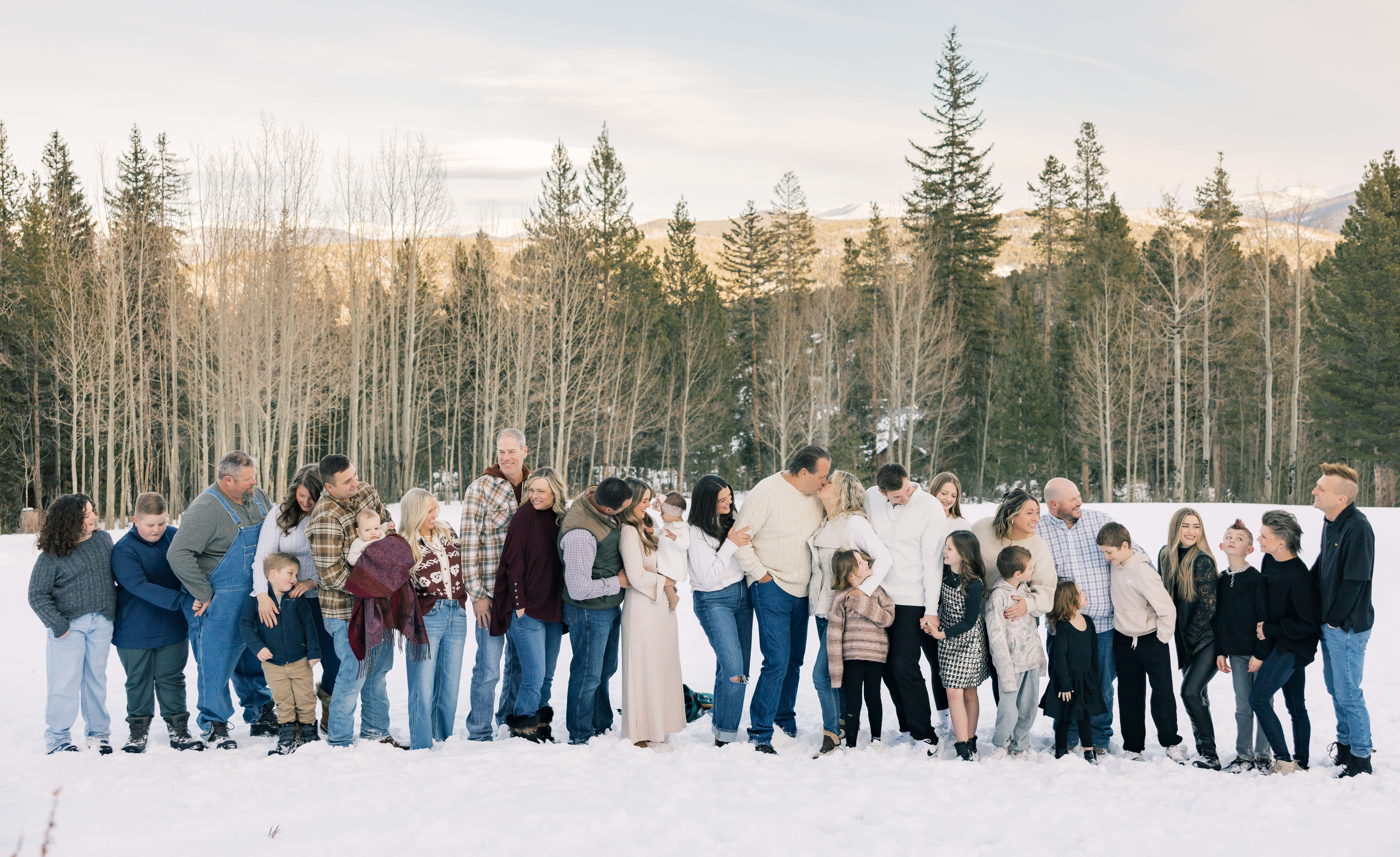 A large extended family laugh and hug each other in a line while standing in a snowy meadow in the mountains while staying at Breckenridge Ski Resort Condos