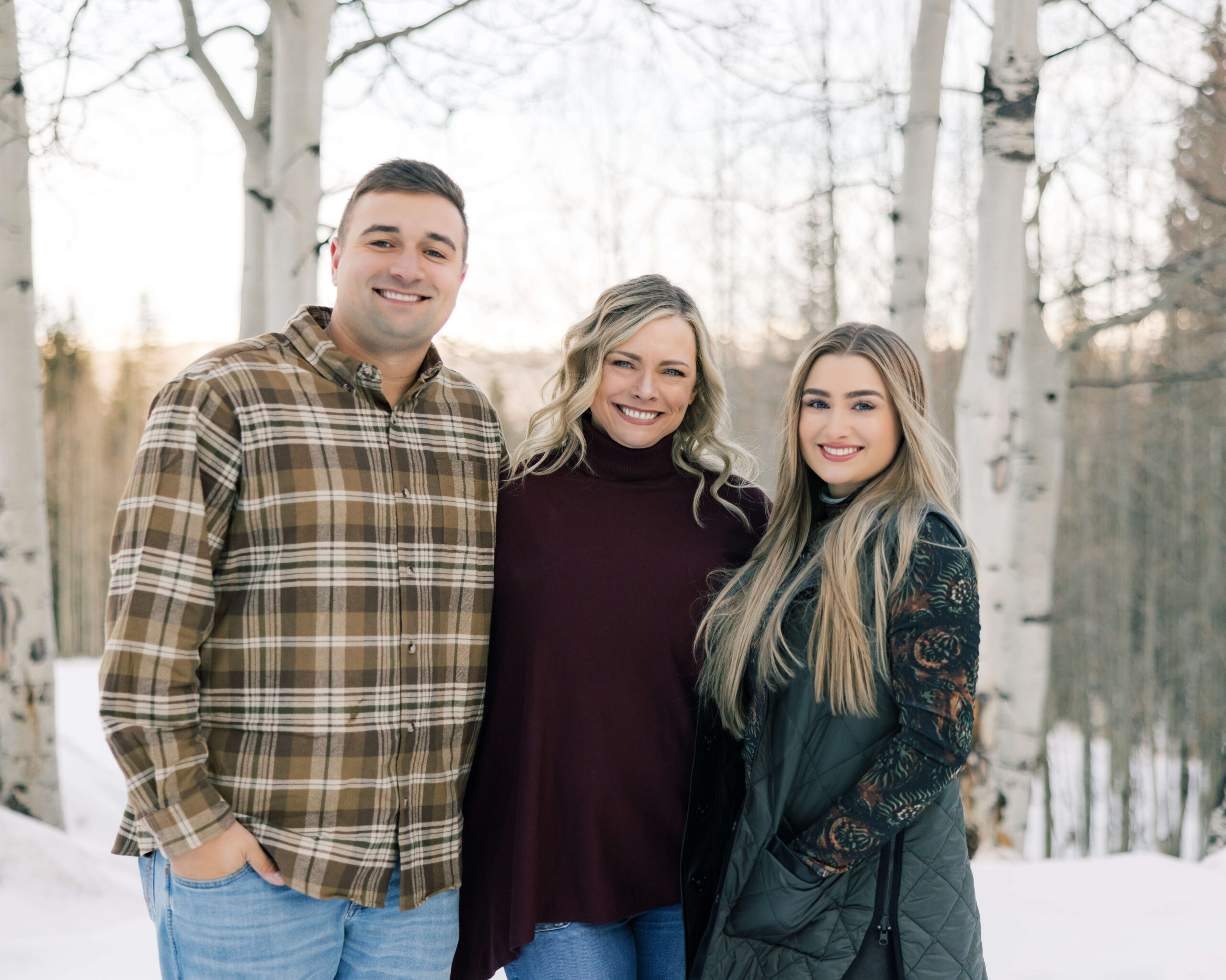 A happy mom stands with her adult son and daughter in a snow covered aspen forest while staying at Breckenridge Ski Resort Condos