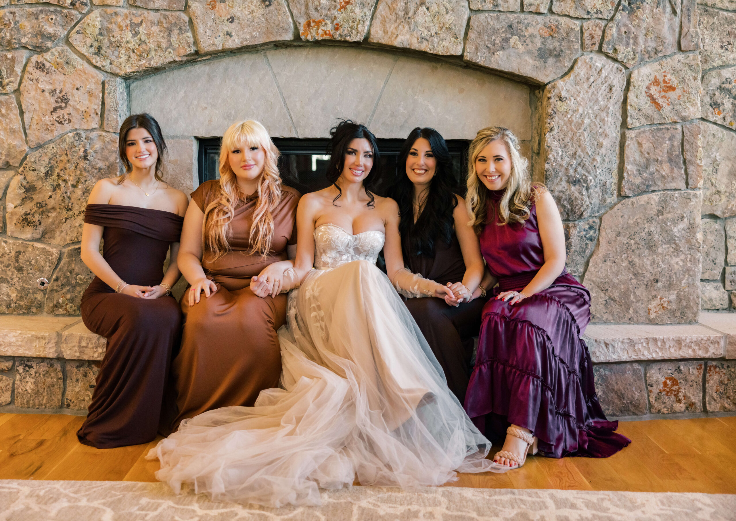 A bride sits holding hands on a fireplace ledge with her bridesmaids at one of the Breckenridge Ski Resort Condos