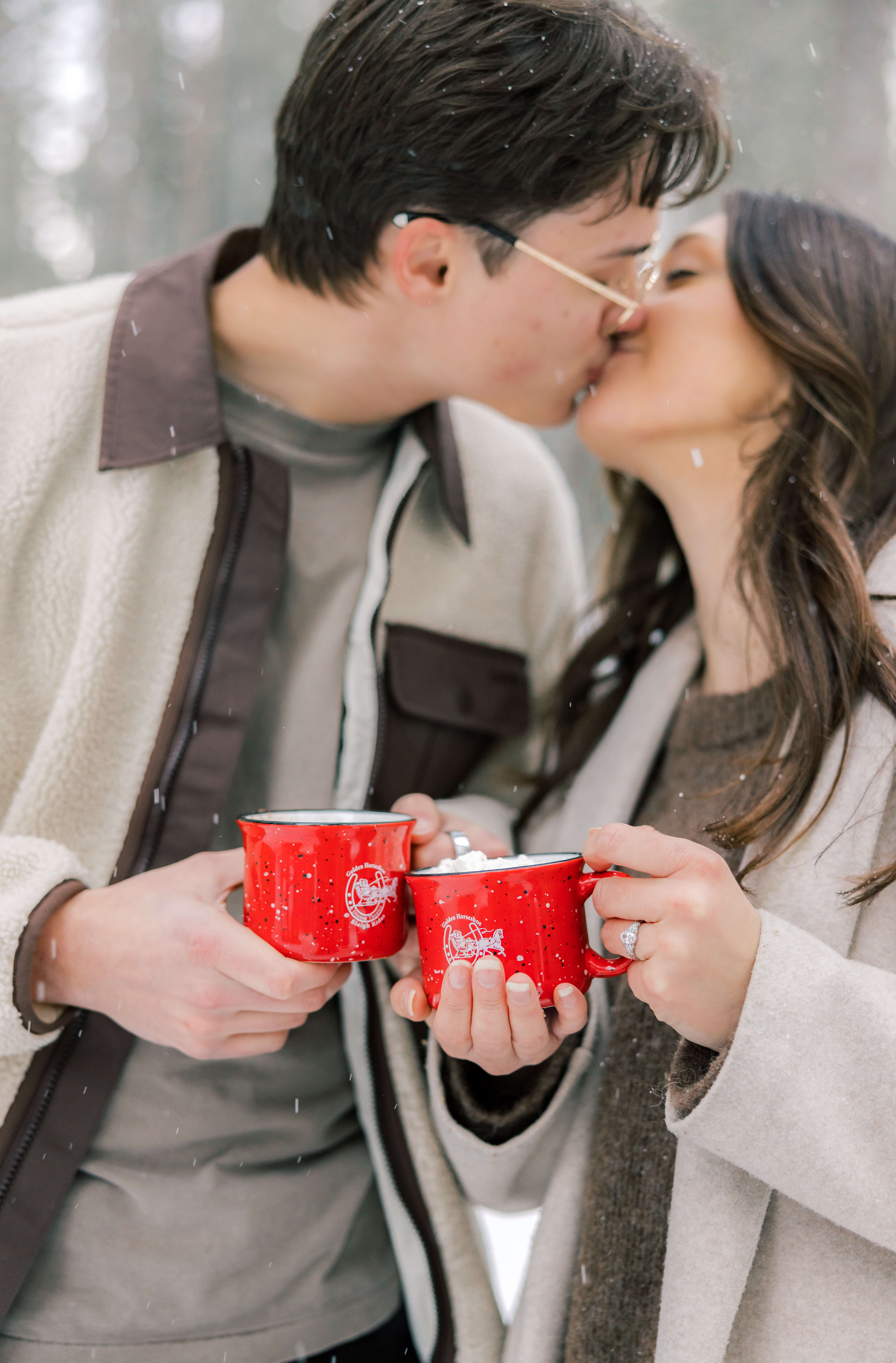 A happy couple kisses while toasting their hot chocolate in the snow during one of the Romantic Things To Do In Breckenridge