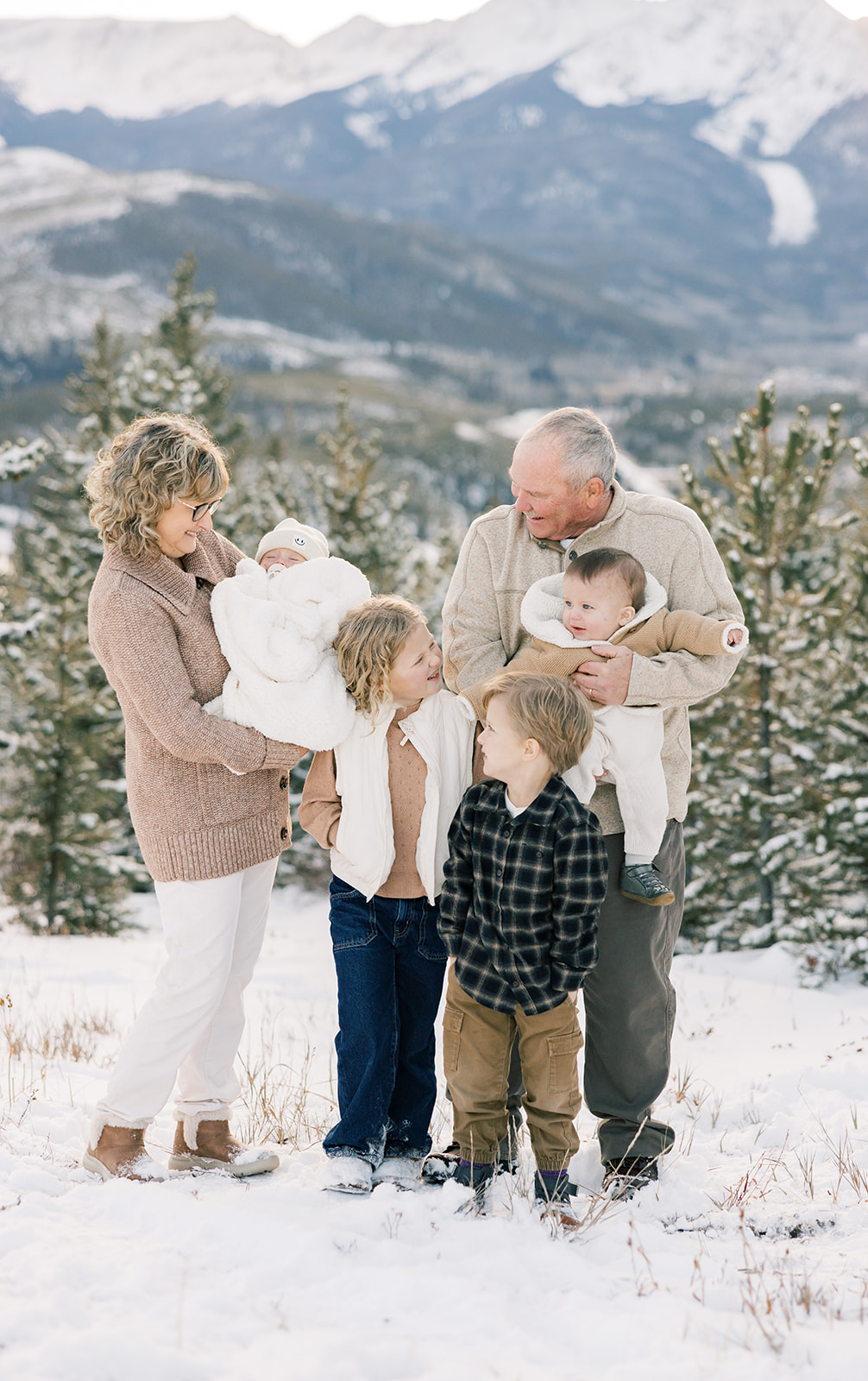 Grandma and grandpa laugh with their four grandkids while holding the two youngest on a mountain in the snow at Breckenridge Fun Park