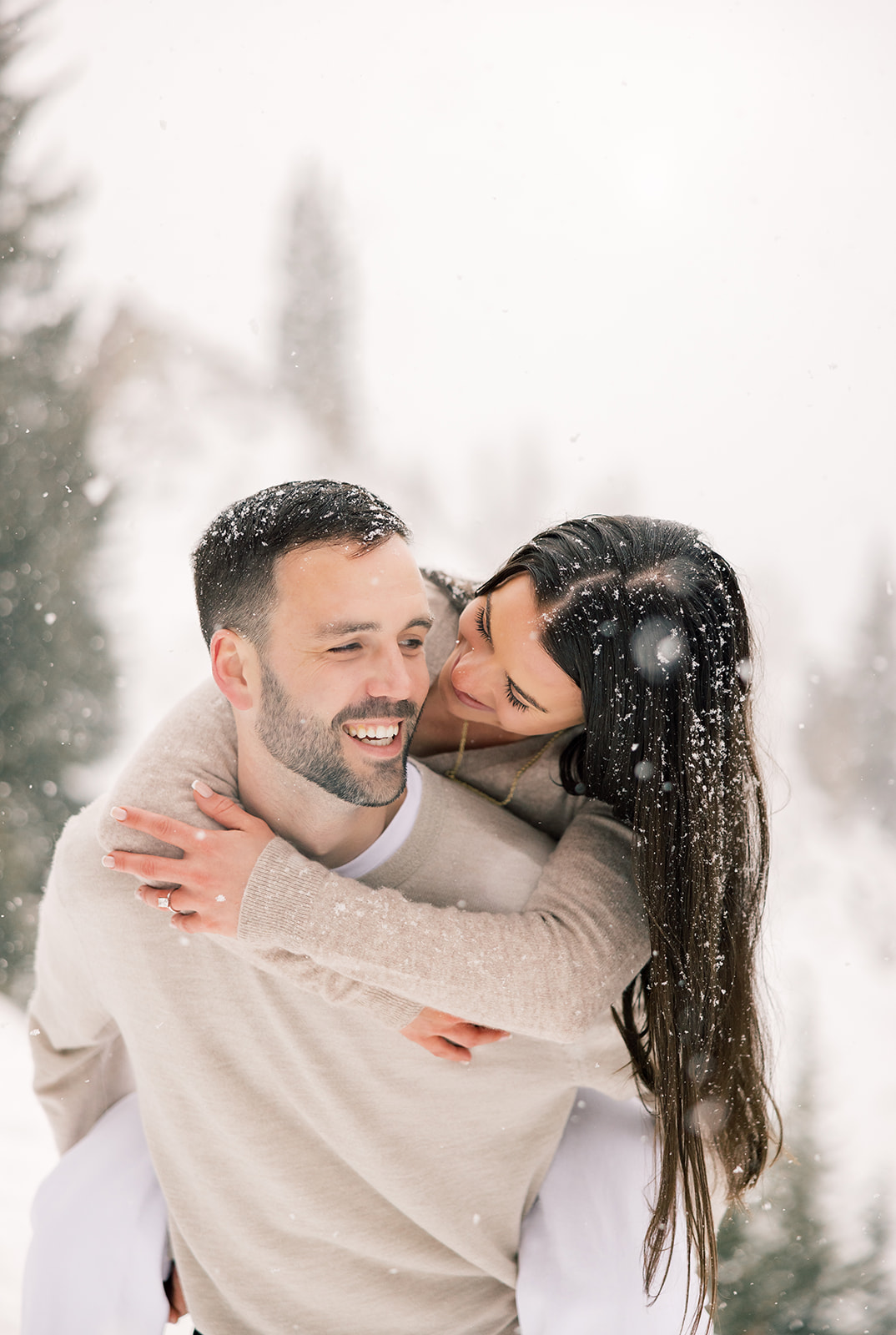 A happy couple in tan play in the snow with a piggy back ride and big smiles after finding brunch in Breckenridge