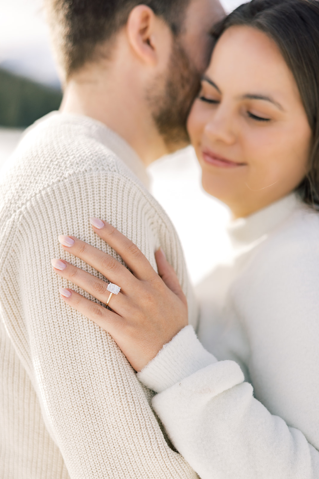 Details of a woman's engagement ring on her finger while hugging her fiancee