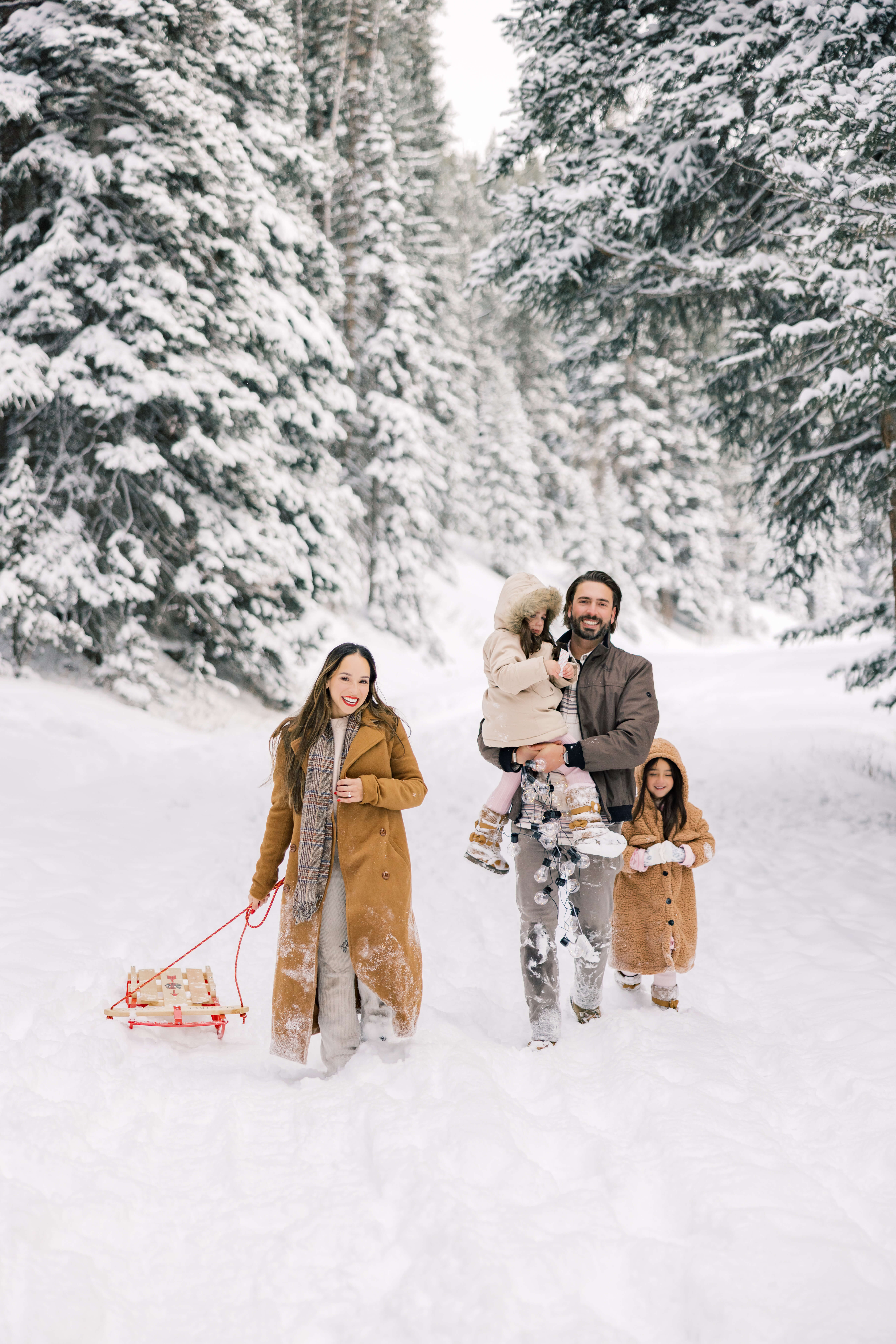 A happy family of three hike through the snow in big coats dragging a sleigh after one of the Tours In Breckenridge
