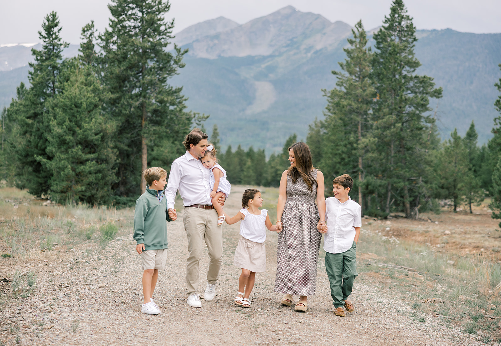 A mom and dad walk a trail holding hands with their four toddler children in a mountain forest