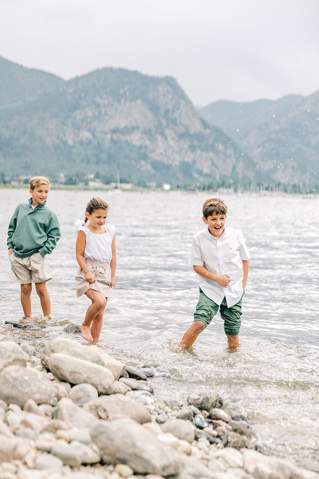 three toddler siblings play in the water in white and green outfits with pants rolled up after visiting arcades in Breckenridge