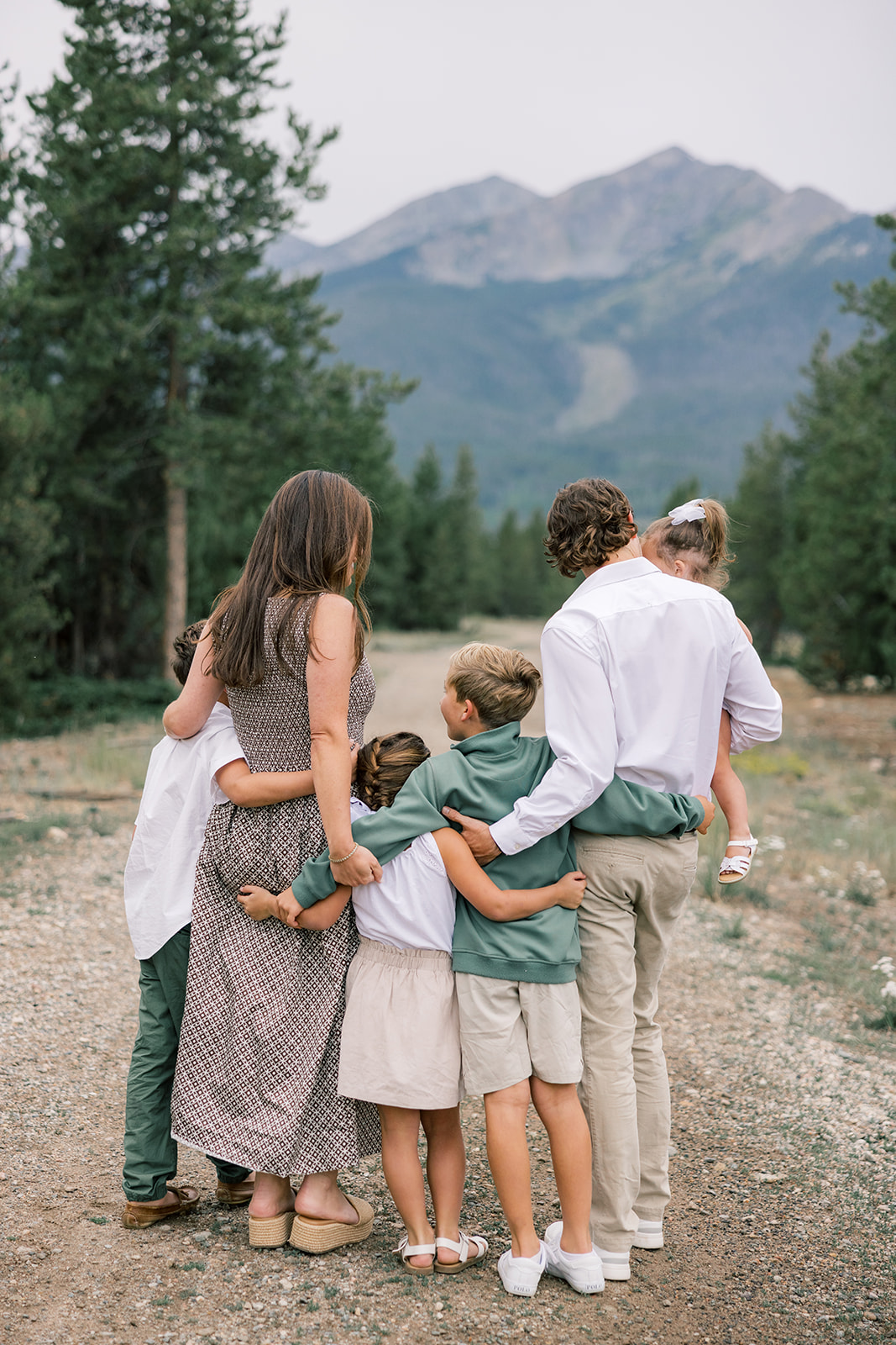 The back of a happy family as they hug and stand in a mountain trail in green and white after visiting arcades in Breckenridge