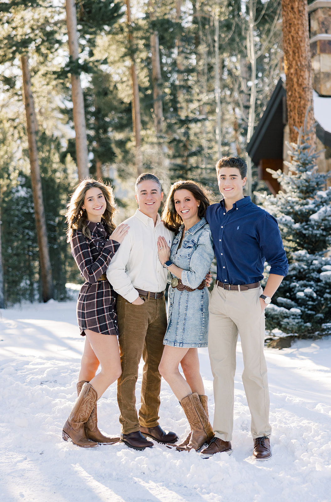 A mom and dad stand in the snow smiling and hugging their teen son and daughter after some outdoor ice skating in Breckenridge