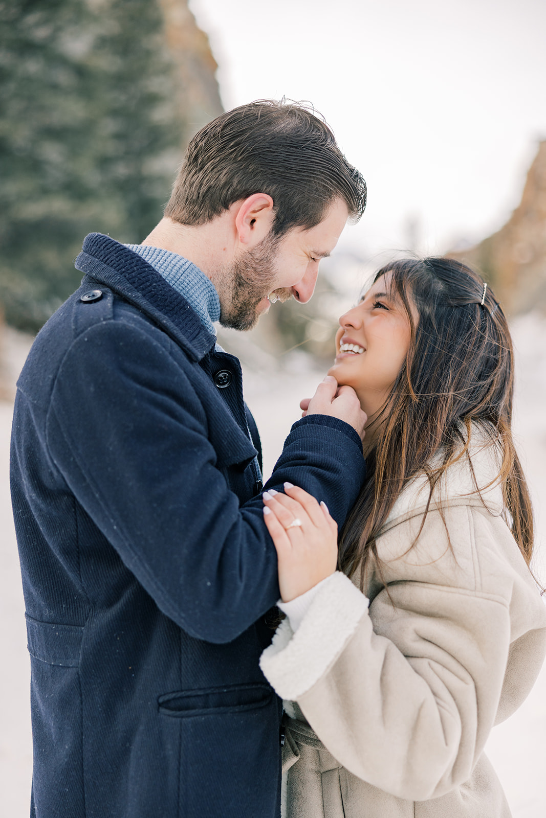 A newly engaged couple smiles at each other while in the snowy mountains in blue and tan coats before heading to things to do in Breckenridge at night