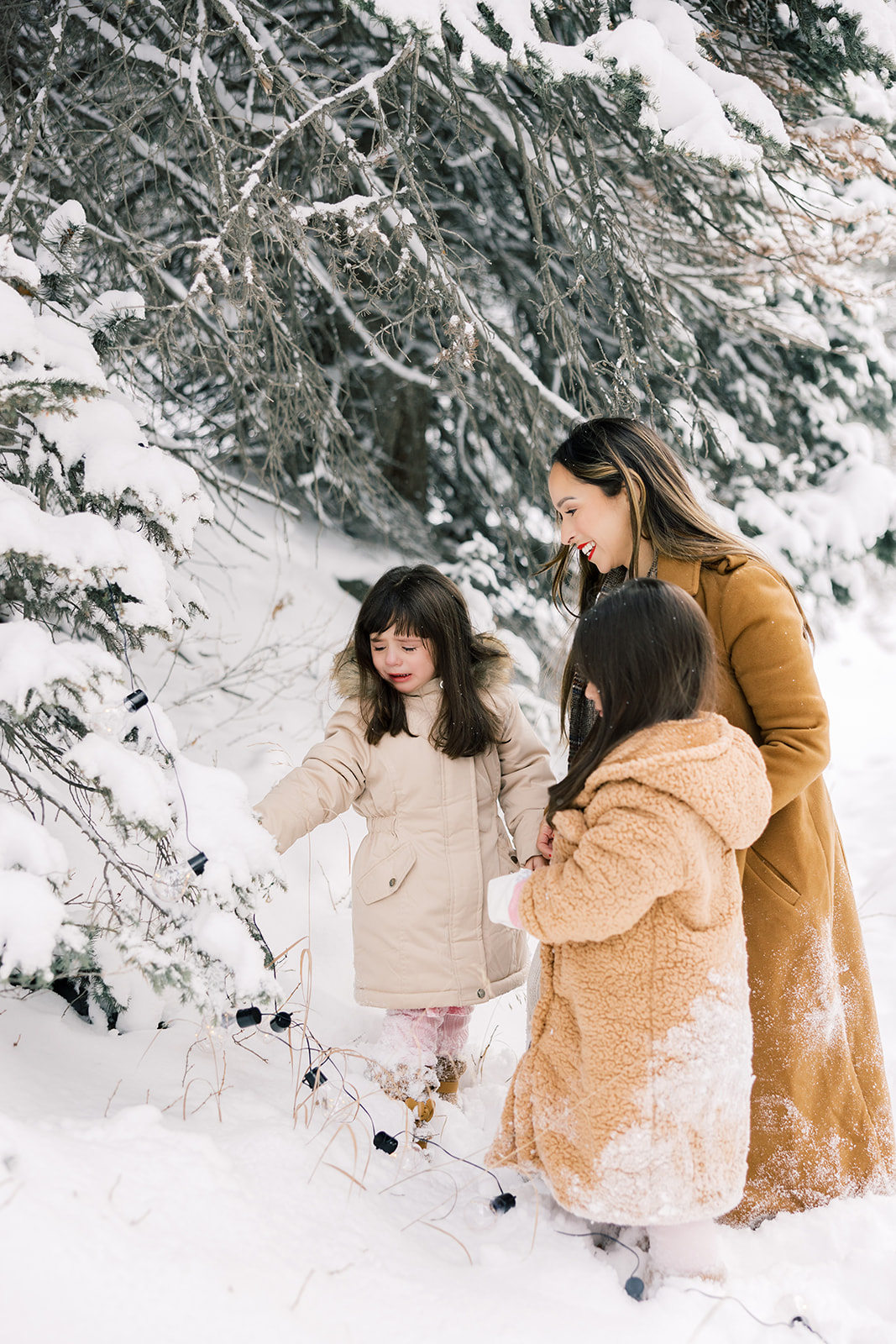 Two young girls explore snow covered mountain trees with mom in big coats after enjoying Breckenridge Ski Resort Child Care