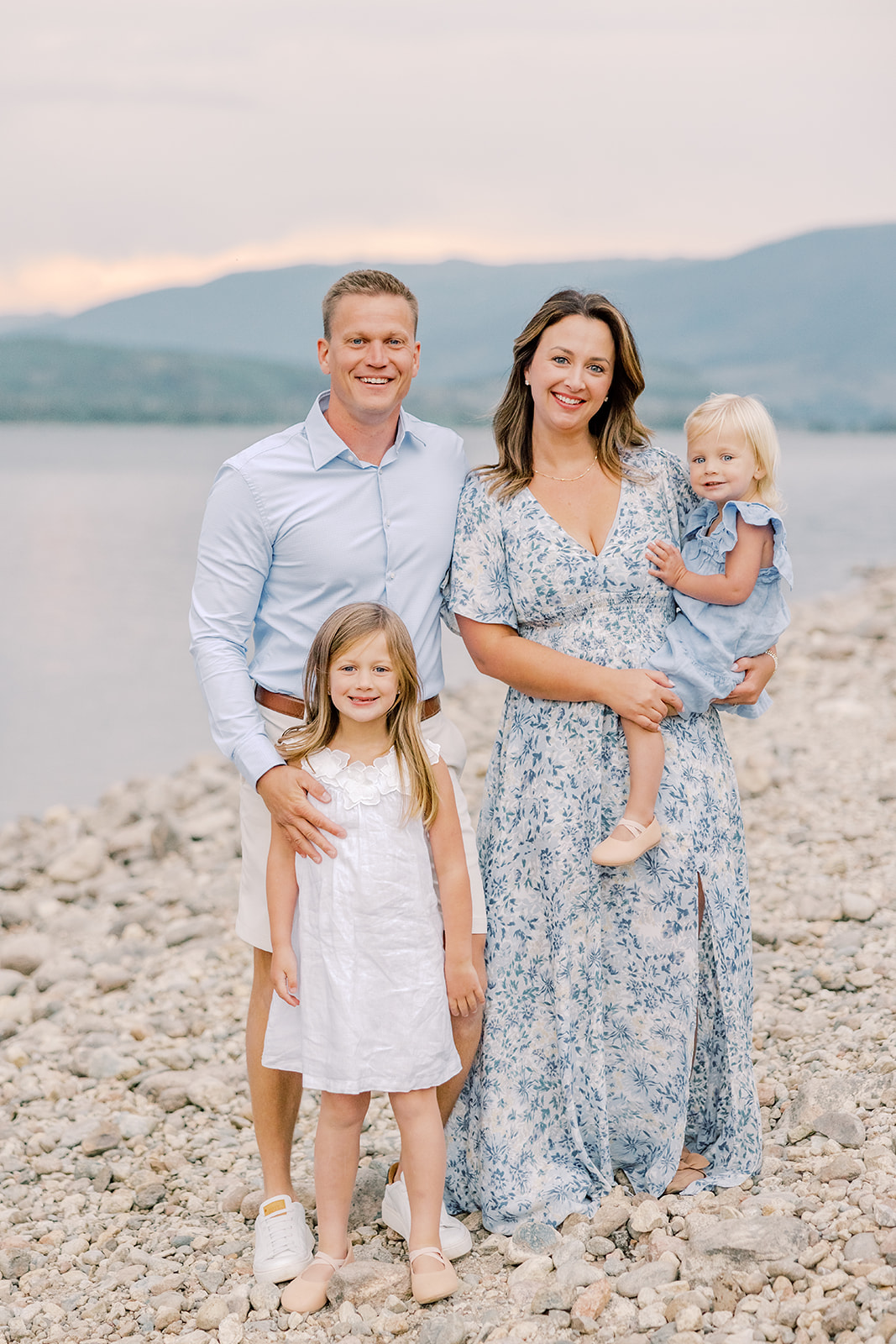 A mom and dad in blue stand by an alpine lake with their two toddler daughters after finding car services in Breckenridge