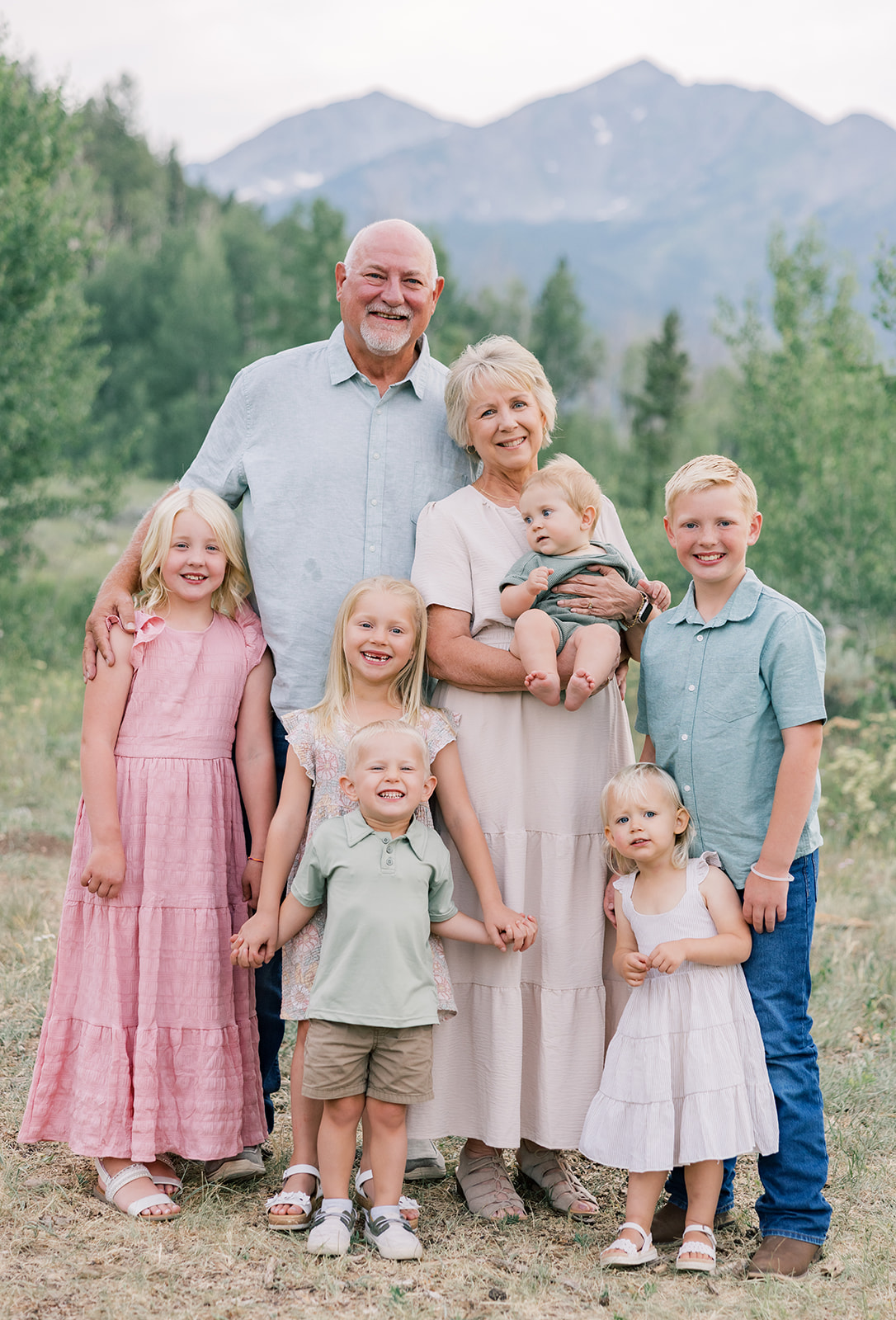 6 siblings smile while standing in the mountains with grandma and grandpa