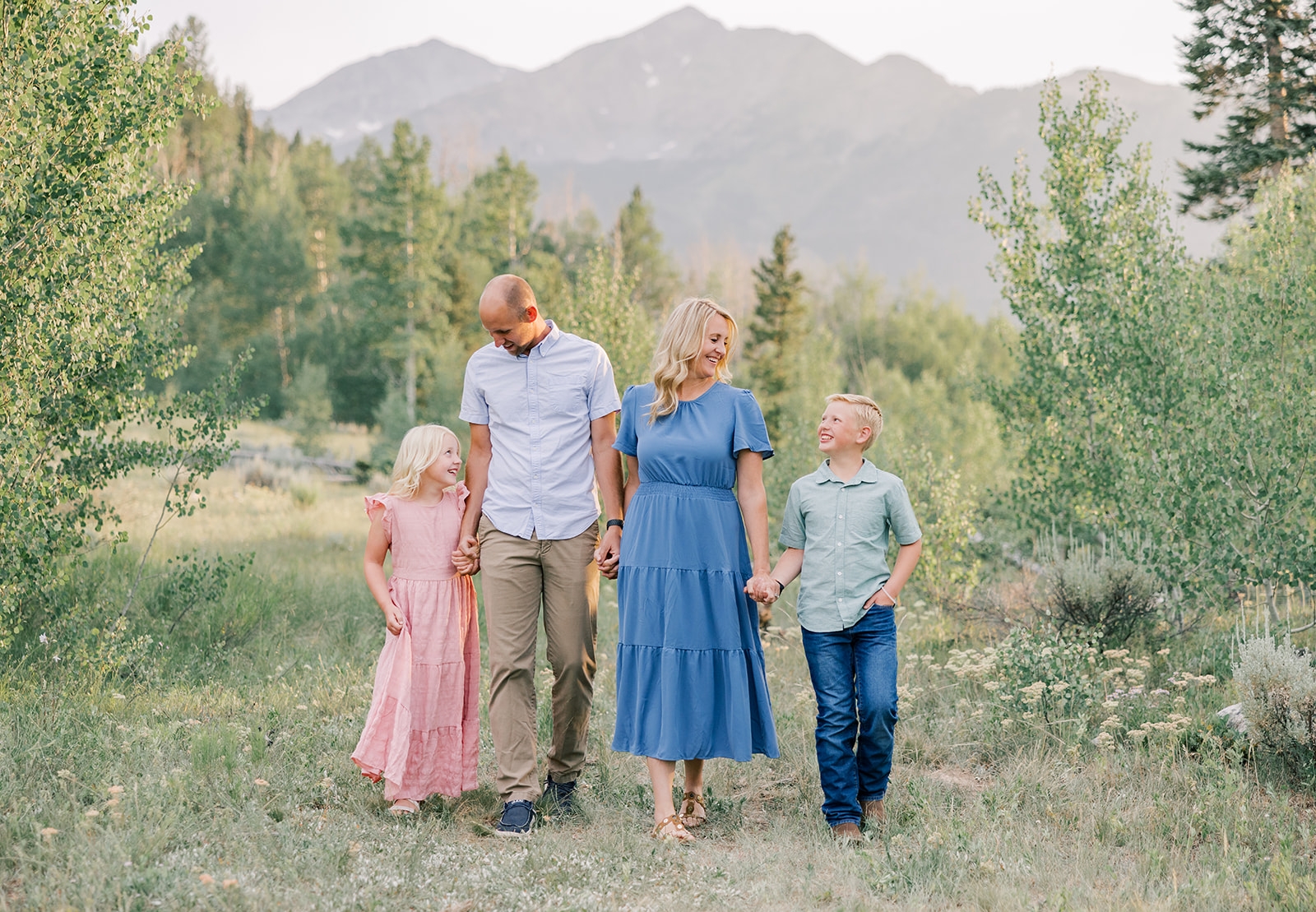 A happy mom and dad in blue walk holding hands and smiling with their toddler son and daughter in a trail after enjoying gold mine tours in Breckenridge