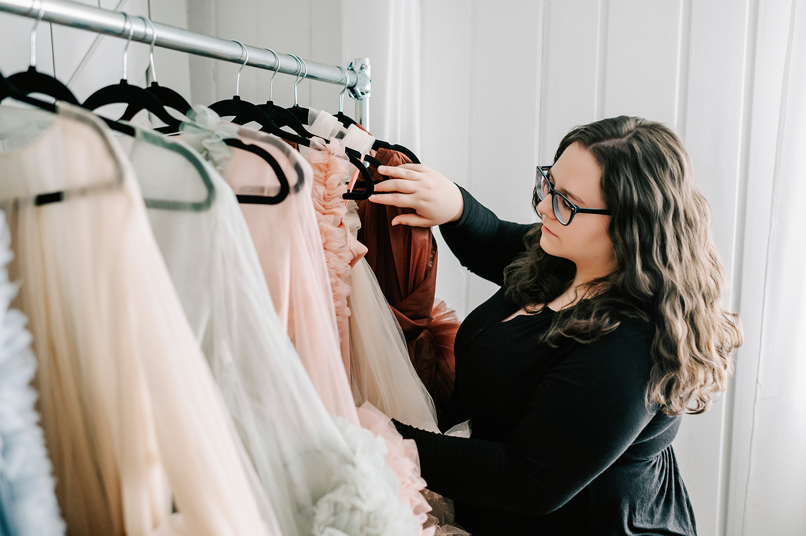 Owner of Mama Bump Rentals sorts through a collection of tulle gowns on a rack
