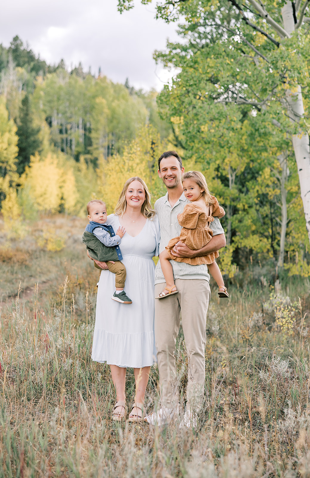 Toddler brother and sister sit on mom and dad's hips while in a forest