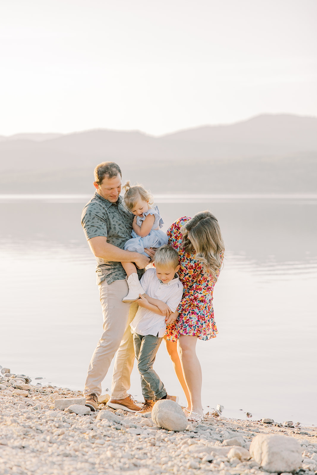 A happy family playing and exploring on a rocky lakeshore at sunset