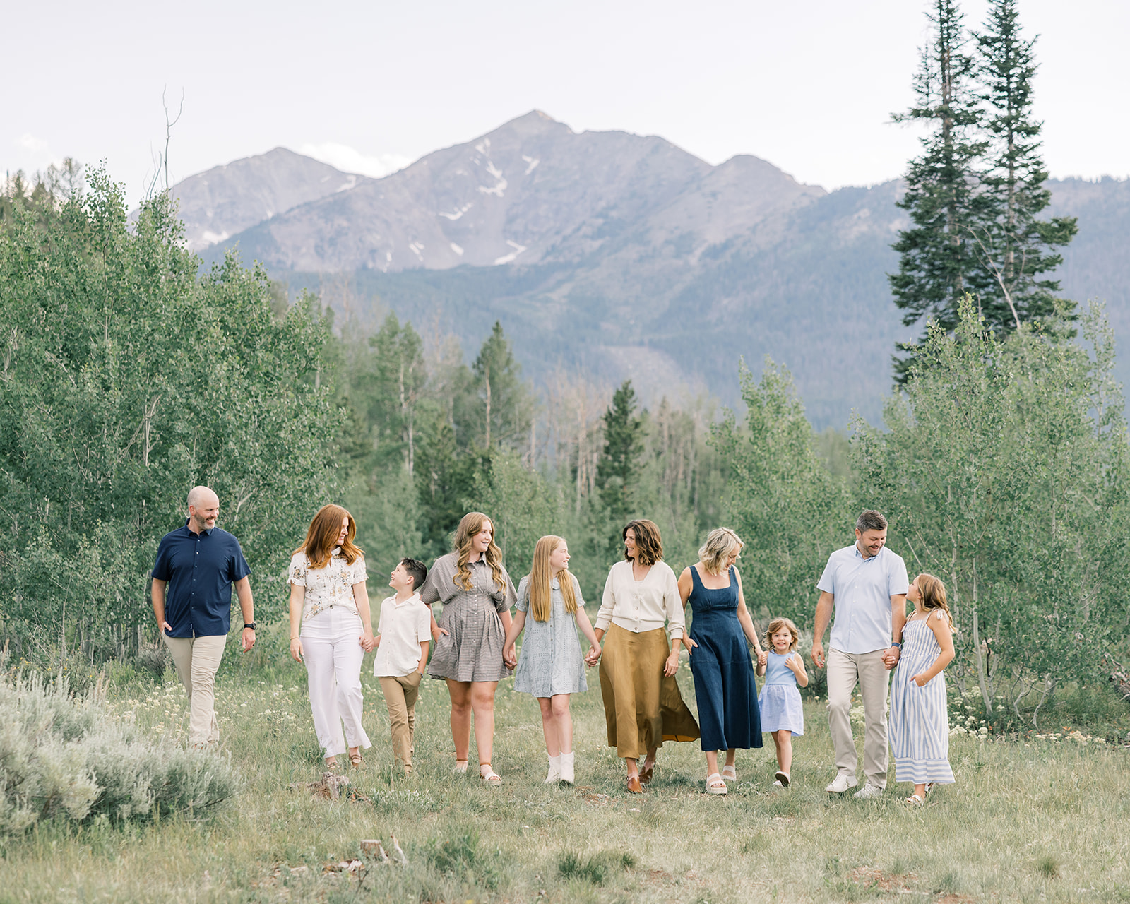 An extended family walks in a mountain trail holding hands and laughing
