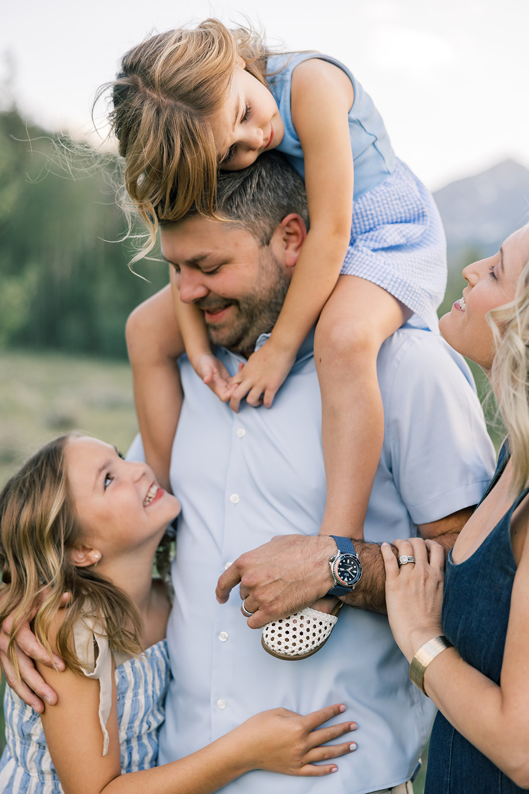 Two happy young girls climb and hug on dad while on a mountain hike in matching blue outfits after finding kid-friendly breweries in Breckenridge