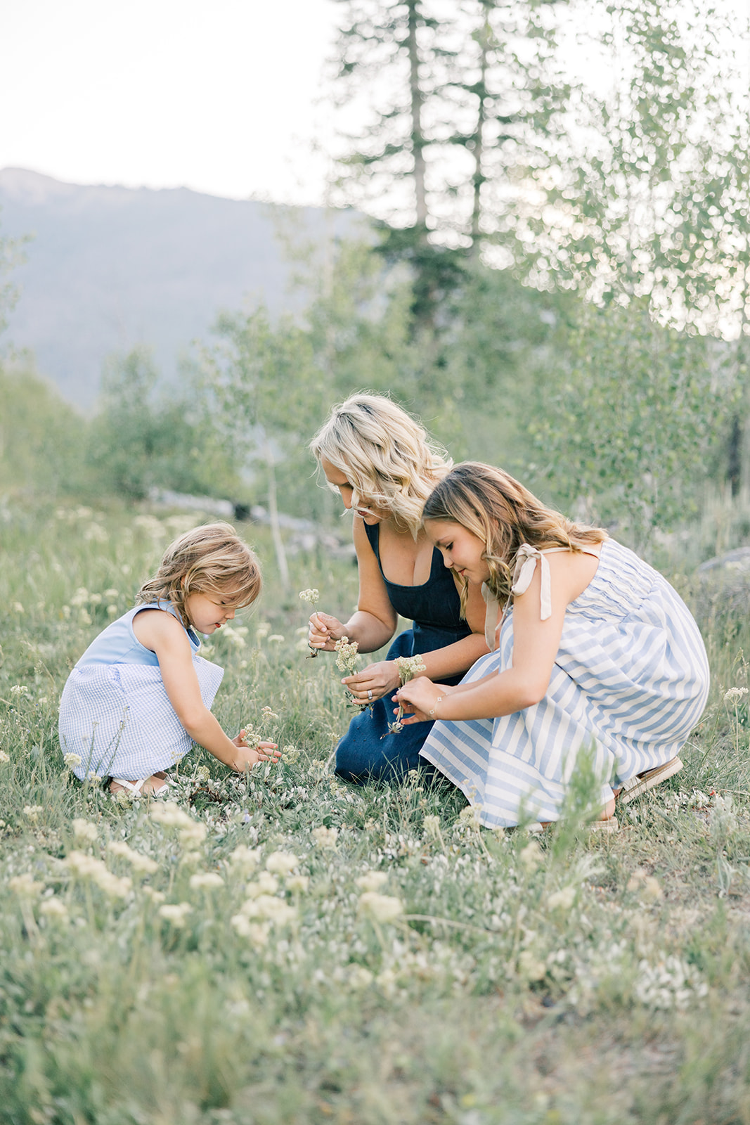A mother picks wildflowers with her two young daughters in blue dresses in a mountain meadow after enjoying kid-friendly breweries in Breckenridge