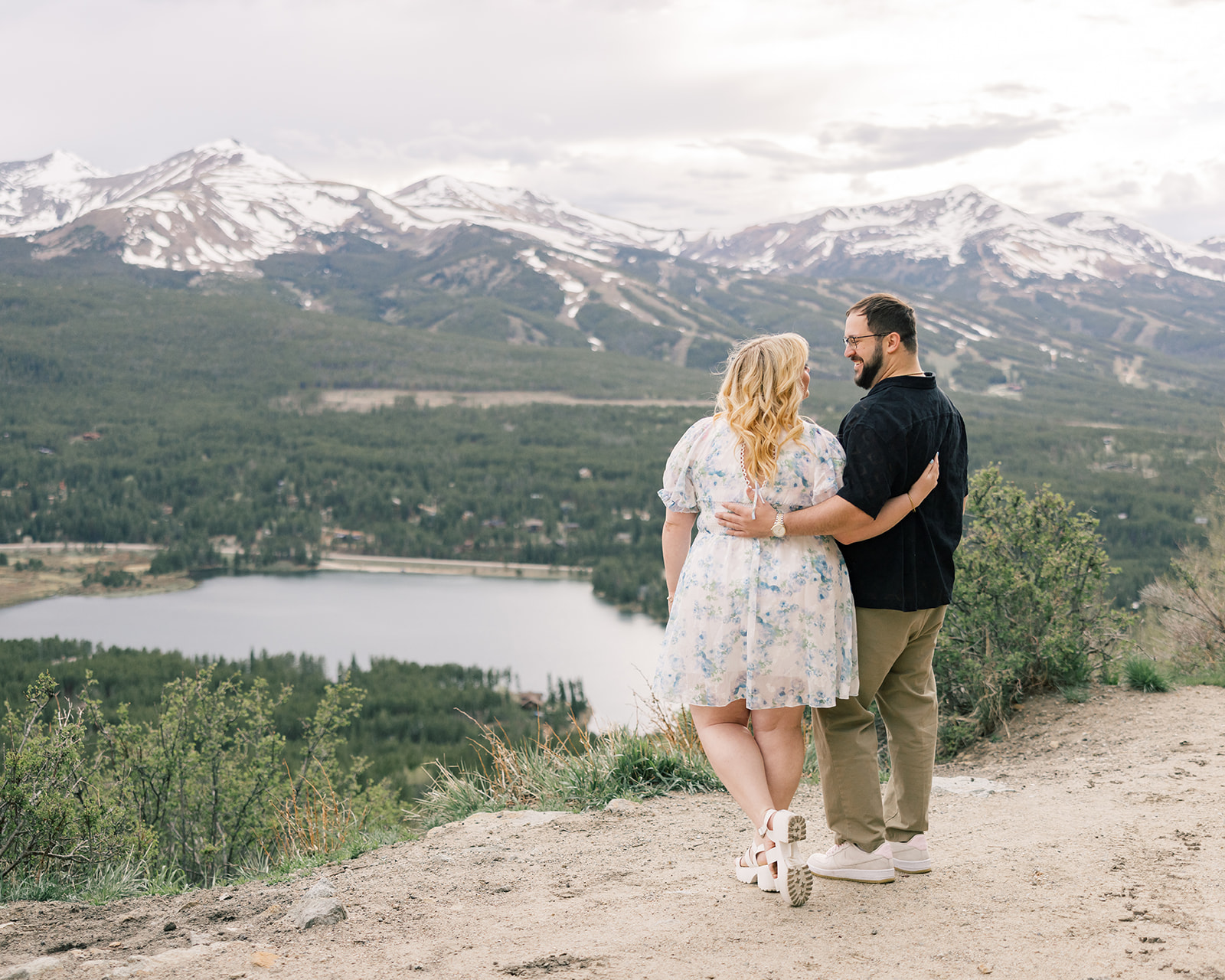 A happy couple in a floral dress and black shirt smile at each other while enjoying a hike and staying at luxury cabins in Breckenridge, CO