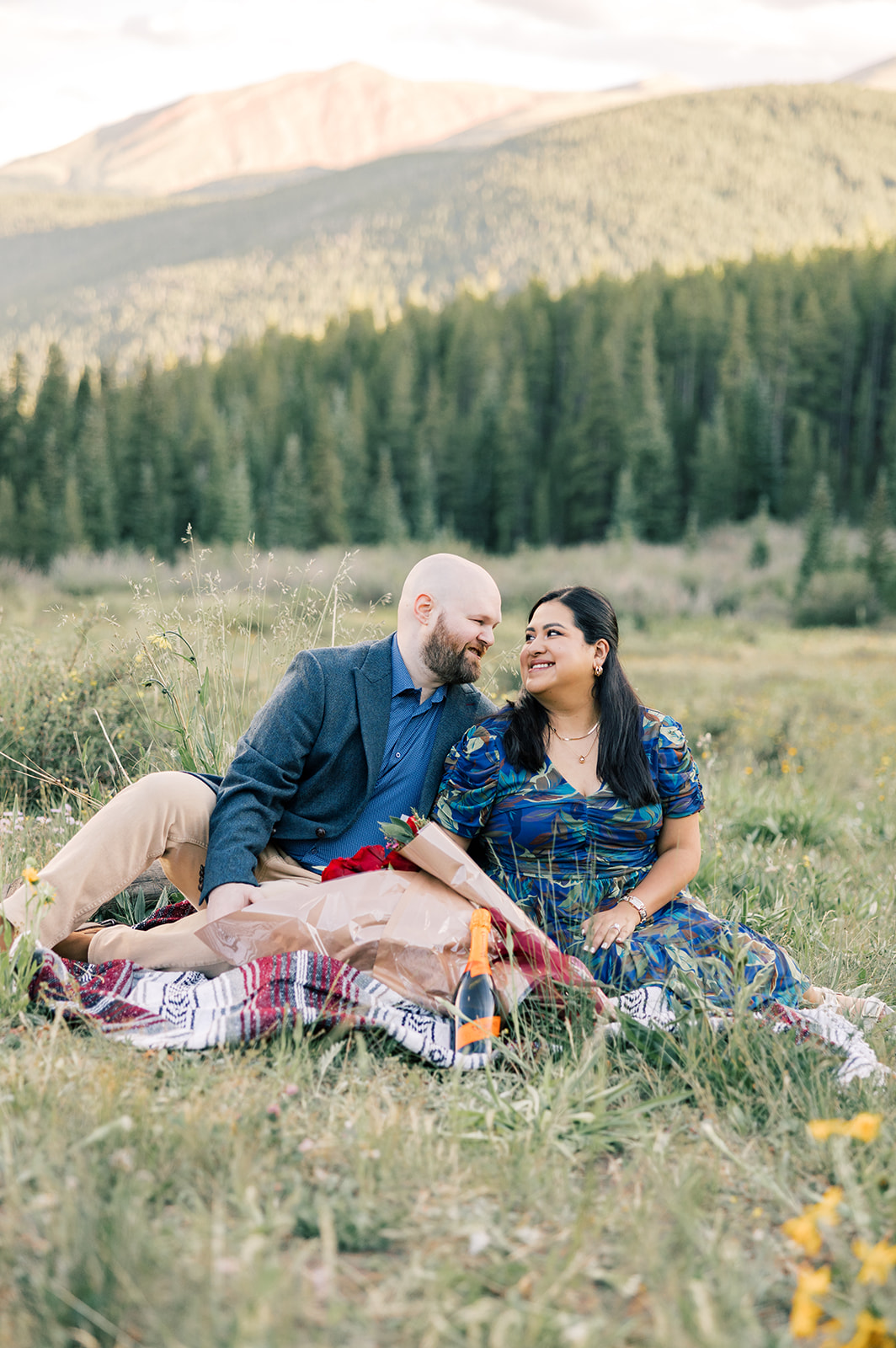 A happy couple in blue cuddle on a picnic blanket in a meadow at sunset after enjoying private dining in Breckenridge