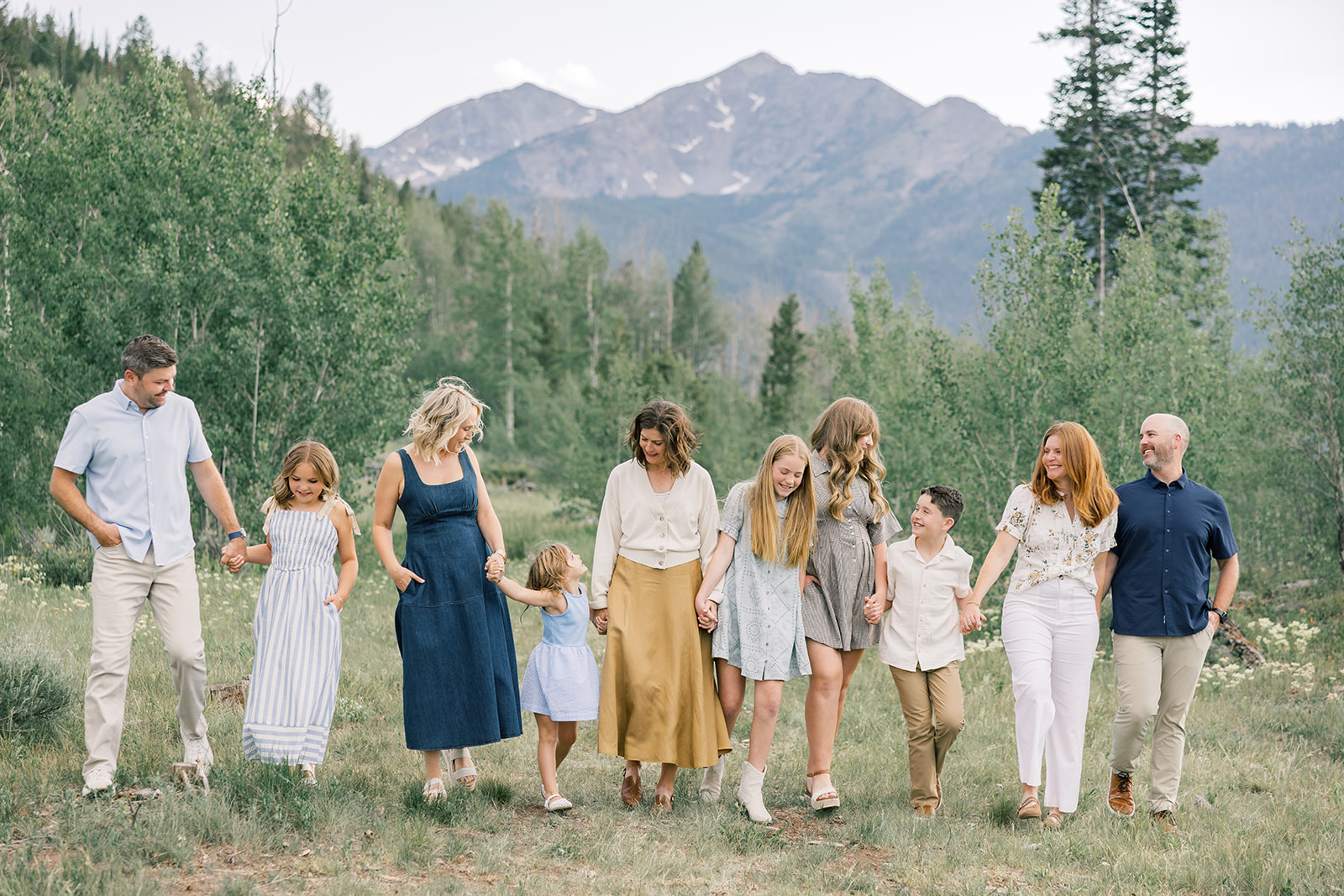 A large extended family walks holding hands in a mountain trail with big smiles while staying at Breckenridge family resorts